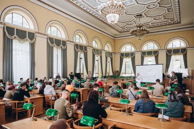 На зображенні представлено простору, урочисту та добре освітлену залу, де проходить презентація фотокниги Костянтина та Влади Ліберових «Очі війни».
