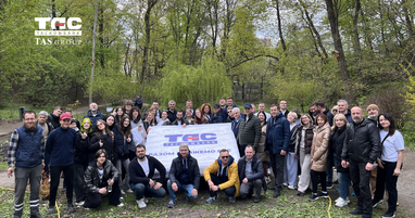 Групповое фото людей на фоне зеленого весеннего парка. Люди позируют вместе, держа большой белый баннер с логотипом банка