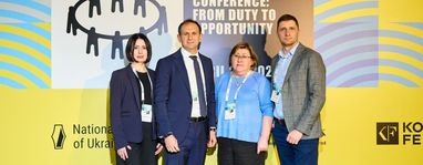 На зображенні представлено офіційне групове фото чотирьох осіб, зроблено на фоні банера конференції.