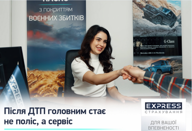 На фото: улыбающаяся женщина-менеджер, что сидит за рабочим столом в офисе и пожимает руку клиенту на фоне рекламных плакатов