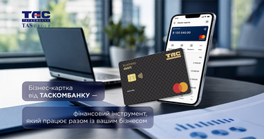 На переднем плане на офисном столе изображена черная дебетовая карта Mastercard и смартфон с открытым банковским приложением, где виден баланс и история операций. На заднем плане — ноутбук и светлое окно офиса.